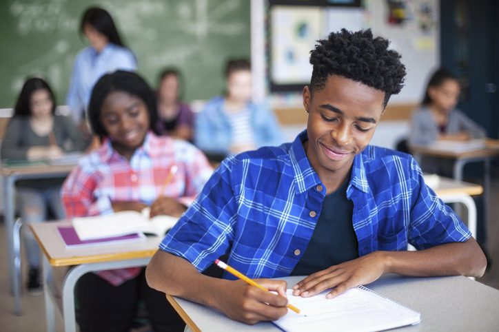 Black ethnicity student writing while studying in classroom